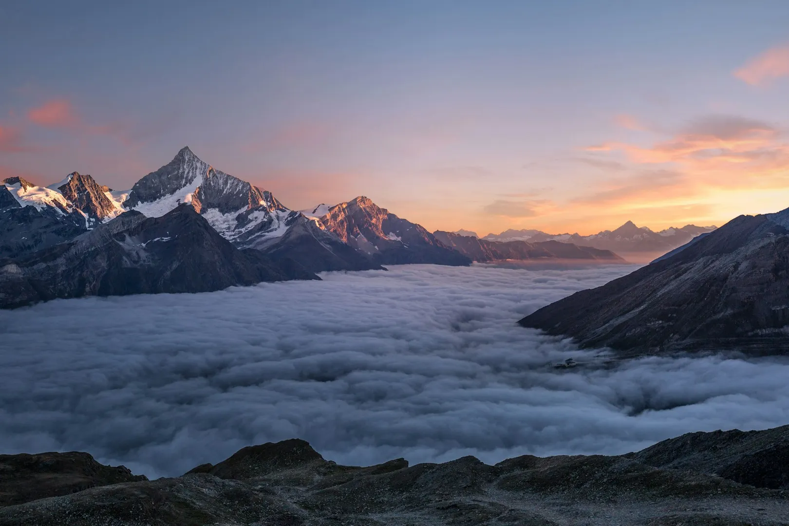 Verschneite Berggipfel über einem Wolkenmeer im Abendrot